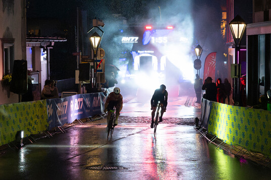 St. Anton Night Sprint Zwei Rennradfahrer rasen durch die Fußgängerzone in St. Anton bei Dämmerung und Regen.